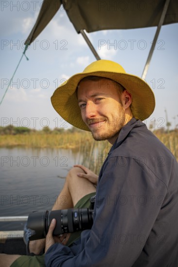 Tourist, photographer, young man with camera on a boat trip, in the evening light, Thamalakane River, Okavango Delta, Botswana
