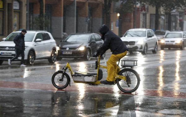 A man rides a cargo bike across a rained road in heavy rain, Berlin, 30.10.2025, Berlin, Berlin, Germany