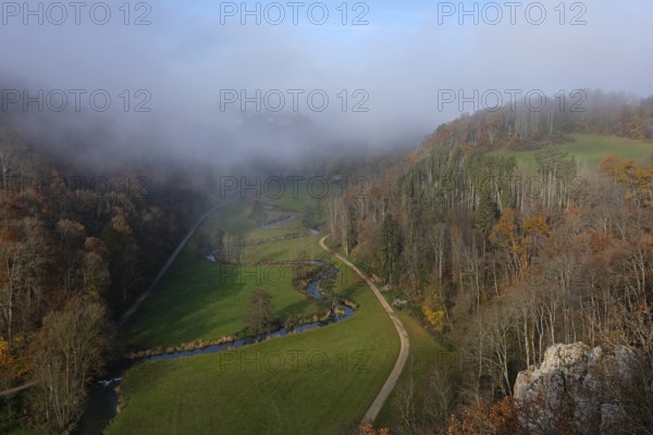 Autumn landscape with rising fog over the Grosse Lauter river loop in Lautertal at sunrise. View from above of the picturesque valley with colorful deciduous forest and rolling hills, Großes Lautertal, Baden-Württemberg, Germany
