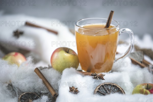 A glass of apple punch with cinnamon sticks and apples in a winter environment