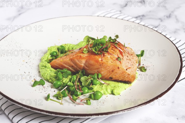Delicious grilled salmon is placed elegantly on creamy green pea puree. Fresh microgreens and peas add a bright touch, creating an appetizing dish perfect for any meal