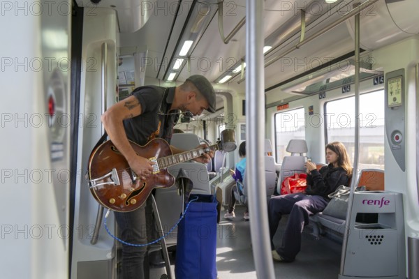 Musician busker playing guitar onboard train of Rodalia de Barcelona suburban rail network, Barcelona, Catalonia, Spain