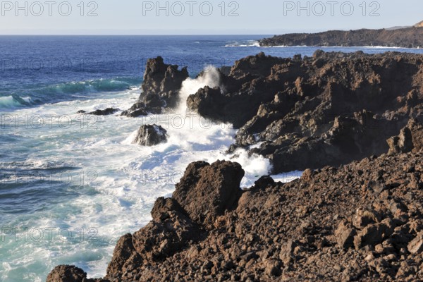 Strong surf claps blazes with white spray white foam from moving sea during swell on rocky coast of sharp-edged lava rock, Lanzarote, Canary Islands, Spain