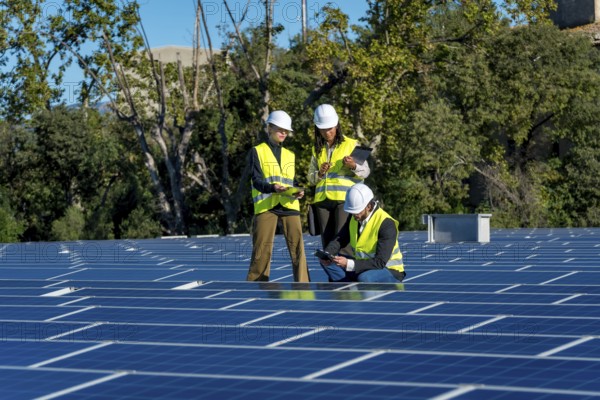 Team of diverse engineers in safety hardhats and vests are collaborating and inspecting the numerous blue solar panels of a large photovoltaic system, working towards sustainable energy solutions