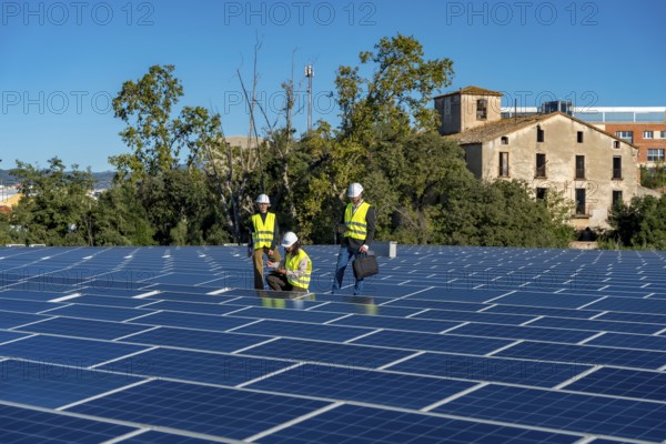 Three engineers wearing safety helmets and vests performing an inspection of a large rooftop solar panel installation, ensuring efficient operation and maintenance of the sustainable energy system