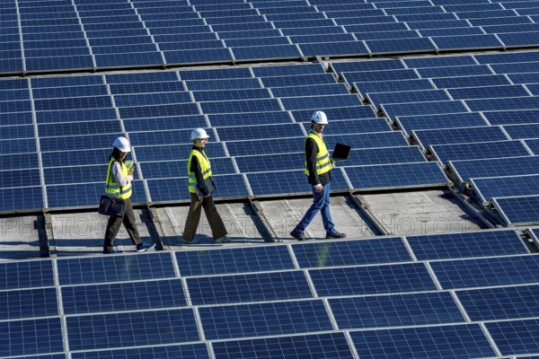 Three engineers walking on a rooftop solar power station, checking and inspecting the large array of photovoltaic panels, demonstrating teamwork in sustainable technology