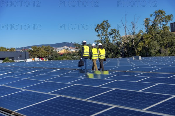 Team of engineers is inspecting an array of solar panels on a rooftop power plant, working on a sustainable energy solution and using renewable technology for electricity production