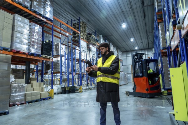 Logistics worker wearing protective clothing, scanning products with a handheld scanner in a modern cold storage warehouse with high racks, implementing advanced inventory management