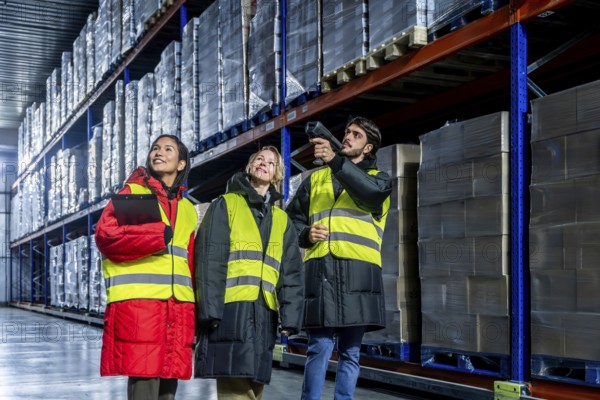 Diverse warehouse team in safety vests and warm protective gear scanning and checking inventory on high racks inside a large cold storage facility, ensuring efficient logistics and distribution