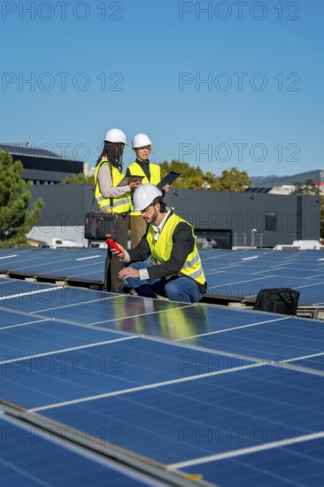Engineers in hard hats and safety vests are examining solar panels on a rooftop, checking efficiency and ensuring proper function of the renewable energy system under a clear blue sky