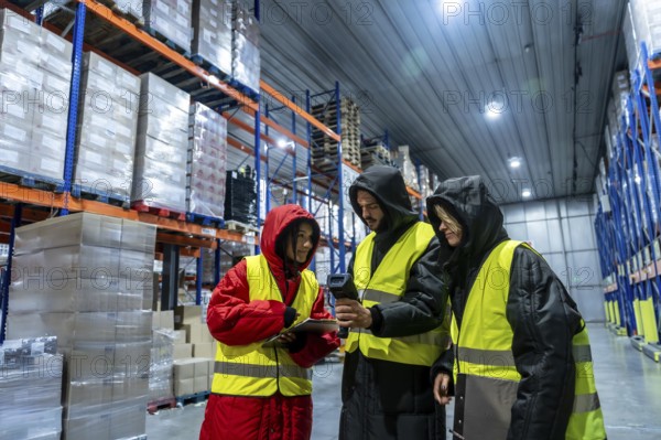 Diverse team in cold storage gear and high visibility vests using barcode scanner and tablet to coordinate inventory and shipments in a large frozen warehouse facility