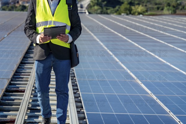 Technician working on a large solar panel installation, reviewing data on a clipboard while walking between rows of photovoltaic modules, ensuring efficient green energy generation