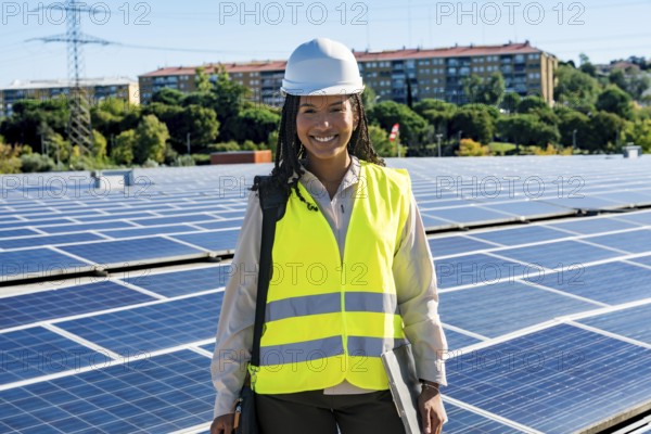 Smiling female engineer standing on a rooftop full of solar panels, wearing a hard hat and safety vest, representing green energy, sustainability, and technological innovation