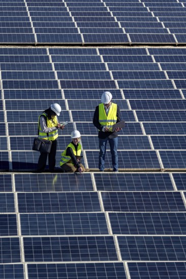 Engineers are inspecting a large solar panel array, focusing on performance and maintenance while working towards sustainable renewable energy and a greener future