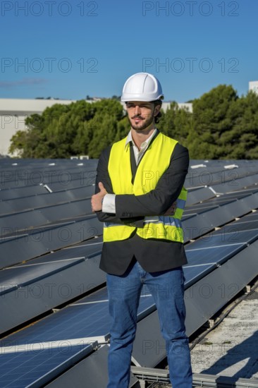 Engineer wearing a hard hat and safety vest standing confidently with arms crossed on a rooftop solar panel array, representing sustainability and green energy development