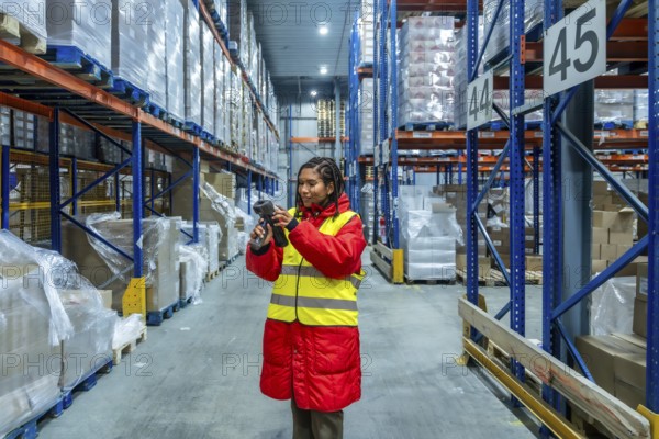Woman worker in high visibility vest and warm jacket scanning pallets of boxes in a cold storage warehouse, managing inventory and ensuring efficient supply chain operations