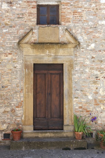 Rustic wooden door in a brick façade with potted plants and a small window above, Tuscany, Italy