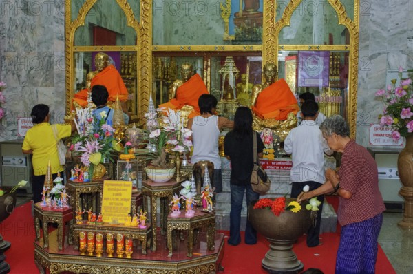 Buddhist believers Buddhists pray making offerings to statues of Buddhist monks covered with gold leaf at Wat Chalong Monastery, Wat Chaithararam, Phuket Island, Phuket Province, Thailand