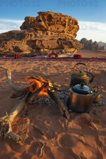 Two teapots next to an open fire in desert sand, eroded rocks in the background, Wadi Rum, Jordan