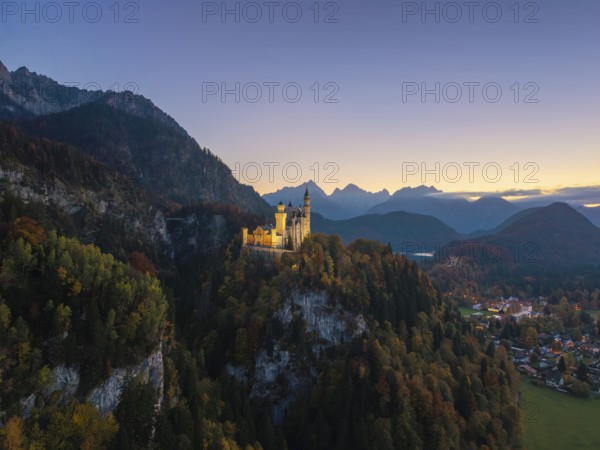 Charming Neuschwanstein Castle in evening light on a dense forest hill in front of impressive mountain ranges, Schwangau near Füssen, Ostallgäu, Allgäu, Bavaria, Germany