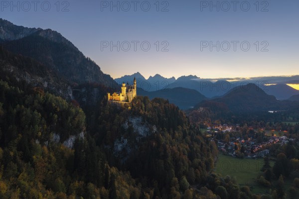 Illuminated Neuschwanstein Castle on hills, surrounded by imposing mountains and an evening atmosphere, Schwangau near Füssen, Ostallgäu, Allgäu, Bavaria, Germany
