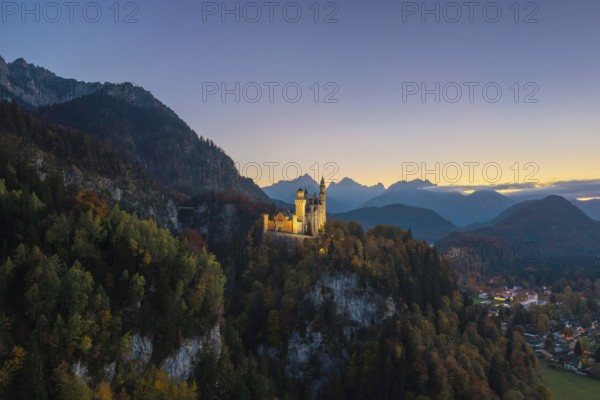 Illuminated Neuschwanstein Castle on a hill with mountain panorama under sunset-drenched sky, Schwangau near Füssen, Ostallgäu, Allgäu, Bavaria, Germany