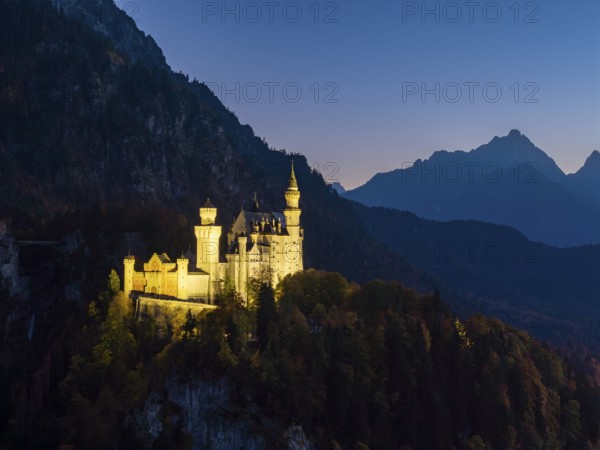 Mysterious view of Neuschwanstein Castle at dusk with mountains in the background
