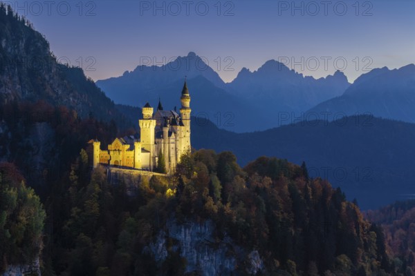 Romantic Neuschwanstein Castle on a hill, illuminated at dusk, with mountains in the background, Schwangau near Füssen, Ostallgäu, Allgäu, Bavaria, Germany