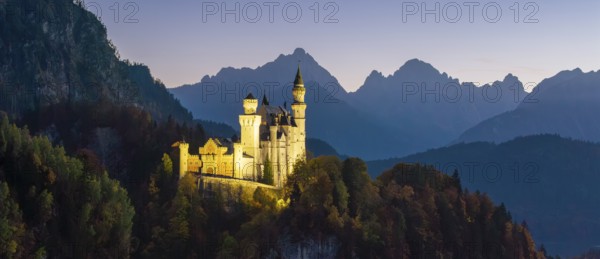 Wide-angle view of Neuschwanstein Castle at dusk and mountains in the background