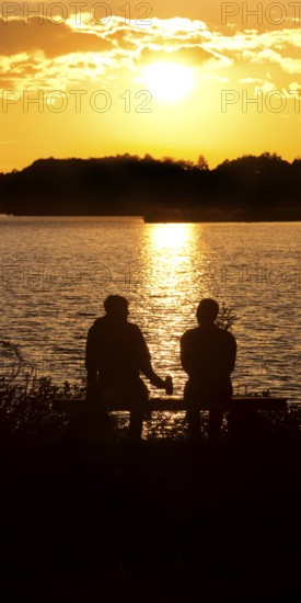 Two men sitting on a bench at sunset at Lake Gudelack, Lindow (Mark), Stechlin-Ruppiner Land nature park Park, Brandenburg, Germany