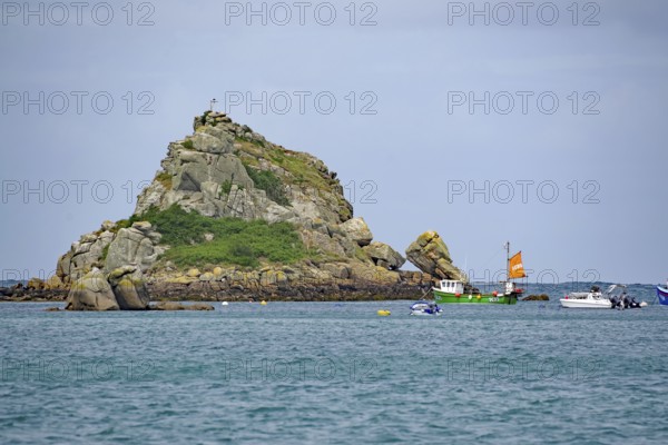 Rocky island with cross and green boat in calm sea under blue sky, Isles of Scilly, Cornwall, United Kingdom