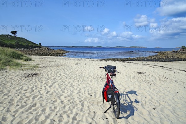 Bicycle on empty sandy beach with views of calm sea under clear skies, St Agnes, Isles of Scilly, Cornwall, United Kingdom