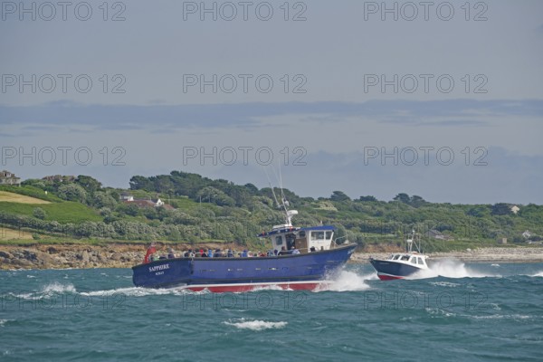Two boats carrying passengers fight the waves near a green coastal landscape, Isles of Scilly, Cornwall, United Kingdom