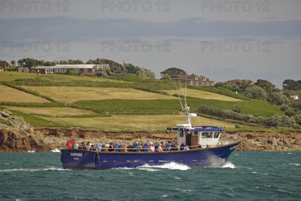 Blue passenger liner sails along a green coastline, Land's End, Cornwall, Great Britain
