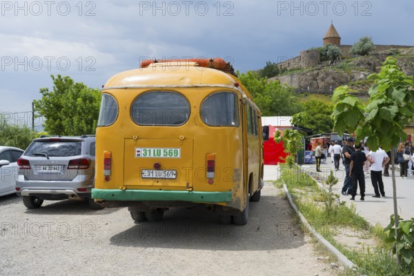 An orange bus from behind, parked next to a busy street with people and buildings, PAZ-672, minibus from the Soviet manufacturer Pavlovsky, gas drive, Khor Virap, Ararat province, Armenia