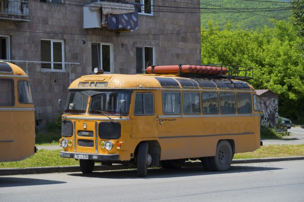 A vintage bus in orange with roof luggage, parked on a street against a green background, PAZ-672, minibus from the Soviet manufacturer Pavlovsky, gas engine, Armenia