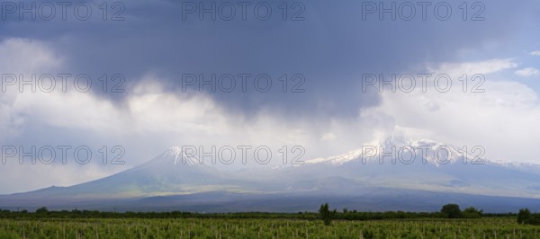 Two snow-capped mountains under dramatic skies with dark clouds over vast fields, Ararat and Little Ararat, located in Turkey, Ararat province, Armenia