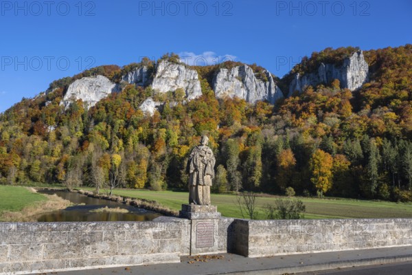 View from the historic arched bridge, Hausener Bridge across the Danube with the statue of Saint Nepomuk, patron saint of bridges, bridge saint, behind them the distinctive Hausener Peaks, climbing rocks, Jurassic limestone cliffs, Weissjura, Jurassic rocks, limestone rocks, surrounded by autumnal vegetation, Hausen im Tal, Upper Danube Valley, Baden-Württemberg, Germany