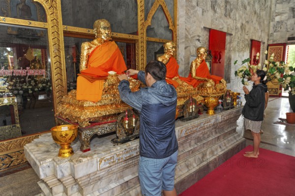 Buddhist believers Buddhists pray making offerings to statues of Buddhist monks covered with gold leaf at Wat Chalong Monastery, Phuket Island, Phuket Province, Thailand