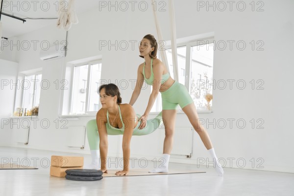 Two women are engaging in a fitness stretching session using a hammock in a bright, spacious studio