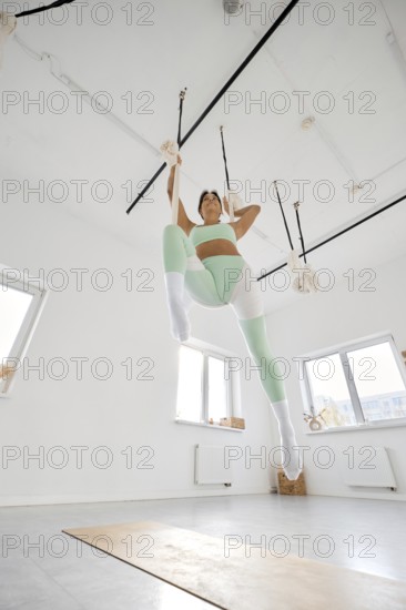 A fitness enthusiast practices stretching techniques with a hammock in a bright and airy indoor space. The activity focuses on enhancing flexibility and strength