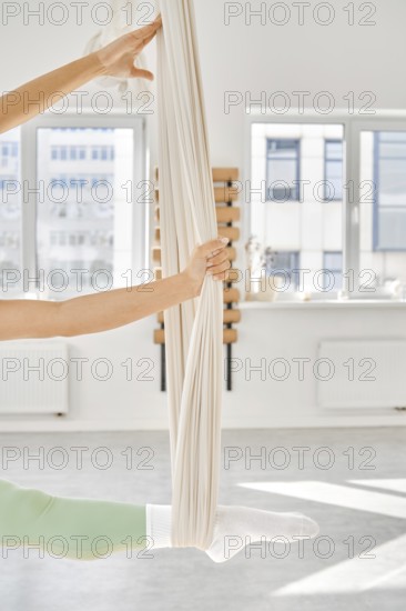 Individual practice stretching exercises using a hammock in a well-lit fitness studio. The scene shows a focus on flexibility as they enhance their strength and balance