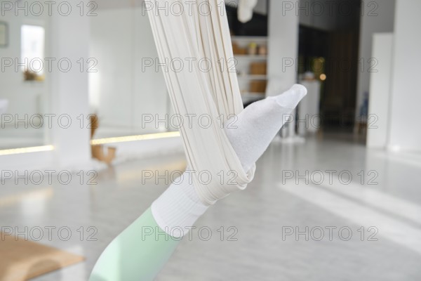 A person engages in fitness stretching using a hammock for support. The scene is set in a bright studio with natural light, enhancing the atmosphere of wellness and relaxation during workout