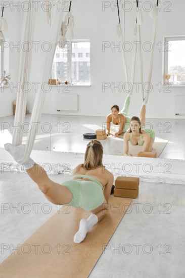A woman is engaged in a leg stretching fitness routine using a hammock in a well-lit studio