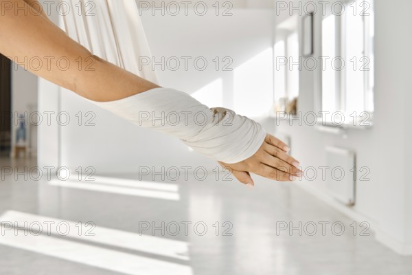 In a spacious room filled with natural light, a person engages in fitness stretching using a hammock. The sunlight casts soft shadows on the floor as they stretch their arm and explore flexibility
