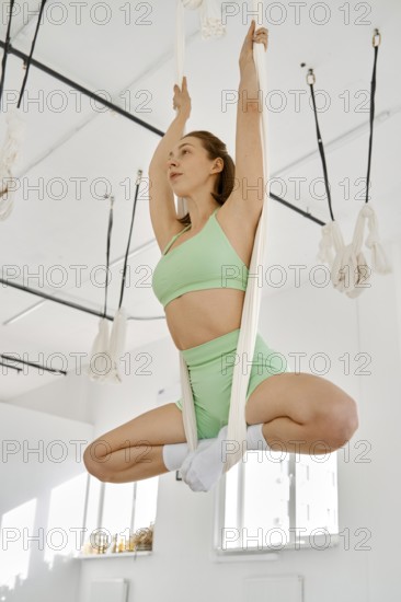 A person practices fitness stretching while suspended in a hammock inside a well-lit studio. The bright environment enhances focus and energy during the workout, adding to the relaxing experience