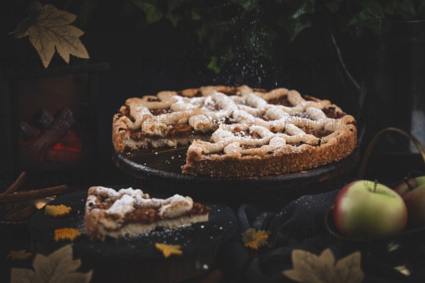 Icing sugar falls on apple pie surrounded by autumn leaves in a dark environment