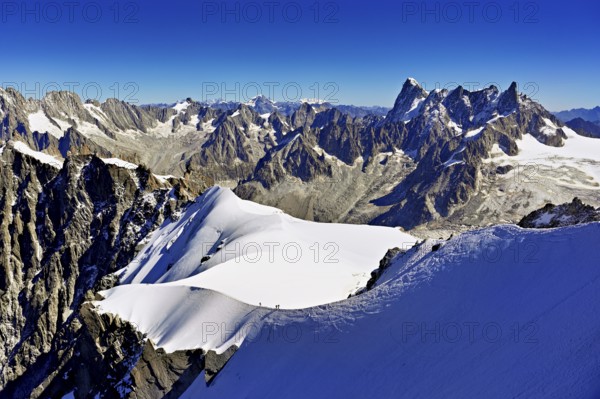 Mountaineers climb over a snow-covered ridge with Grandes Jorasses mountain in the background, Aiguille du Midi mountain station, Chamonix-Mont-Blanc, Haute-Savoie, France