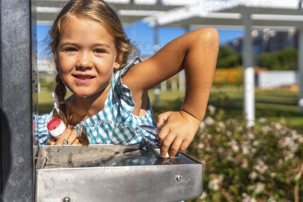 Young child refreshing herself with a drink of water from a public fountain in a sunny park, staying hydrated during summer outdoor activities and smiling at the viewer