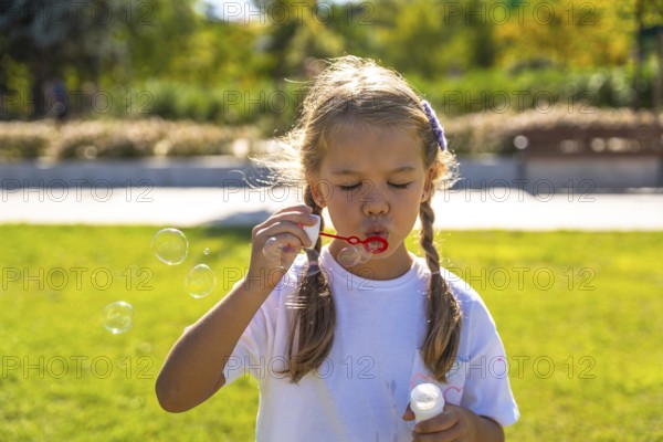 Little girl enjoying outdoor activity, blowing iridescent soap bubbles, experiencing joy and carefree childhood moments during summer holiday in a green park